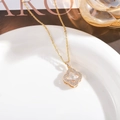 Macro shot of gold four-leaf clover necklace with pave setting on white ceramic tray - White