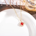 Close-up of golden four-leaf clover pendant with red core and zircons on a white plate - Red