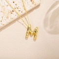 Dettaglio della collana con lettera M dorata e diamanti lucenti su sfondo di pietra - Stile Lettera M (M)