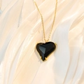 Detail view of a black faceted heart pendant with a gold chain on white silk background - Black