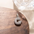 Detailed view of silver letter G pendant with micro-pave cubic zirconia on wooden tray - Letter G