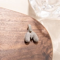 Macro detail of silver bubble letter M pendant with pave-set zircon on wood texture - M