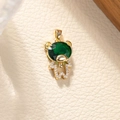 Dettaglio di un ciondolo a forma di orso dorato con gemma verde e cristalli bianchi - Verde pavone