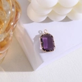 Detalle de un colgante de cristal rectangular morado en montura dorada sobre bloque blanco - Violeta