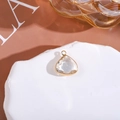 Detail of a pear-shaped crystal pendant with gold plating on a white stone pedestal - White