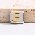 Macro view of stainless steel Italian charm link with gold embossed letter E module - Letter E