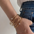 Golden multi-layer wavy open bangle with clear zircon stones on a model wrist - Infinity Rhinestone Inlaid Style (HS1974-2)