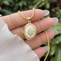 Macro shot of gold oval locket necklace with starburst design and white zircon inlays - 18K Gold / White