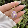 Detailed macro view of an oval purple enamel locket necklace with floral engraving - 18K Gold / Purple