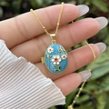 Macro shot of 18K gold plated oval locket featuring blue enamel and delicate floral motifs - 18K Gold / Sky Blue