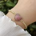 Primer plano de pulsera de cuentas doradas con un colgante de corazón magenta en pavé - Rosa rojo