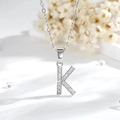 Dettaglio macro di un ciondolo a lettera K in argento con zirconi su una catena chic - K-Argento