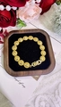 Detailweergave van de gouden koperen armband met ronde schakels op een houten plateau - Goud Rond Midden Reliëf (PSL130)