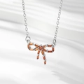 Gros plan du pendentif nœud argenté orné de pierres orange sur un tissu blanc ondulé - Argent / Zirconia Rouge