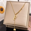 Macro detail of a gold letter F pendant necklace with a tassel cube charm in a gift box - Letter F