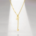 Detail of gold letter K tassel pendant on Y-shaped necklace with polished metal bar links - Letter K