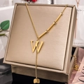 Detail of gold letter W pendant on asymmetric chain displayed on a jewelry box - Letter W