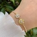 Detailed view of an 18K gold plated bracelet with zircon flowers and heart charms on wrist - White