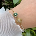 Detailed close-up of a gold-plated bracelet with zircon flower and heart charms on a wrist - Green