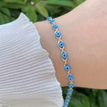 Close-up of golden evil eye bracelet with blue beads on a woman wrist in nature - Bracelet / Blue
