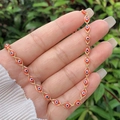 Detailed close-up of a 18K gold-plated chain with red evil eye charms held in hand - Necklace / Red