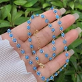 Detail of 18K gold-plated Evil Eye necklace and bracelet set held against nature - Necklace And Bracelet / Blue