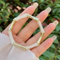 Detailopname van de bamboe-stijl hars armband in parelwit en goud om de pols - Wit (Gouden Knoop)