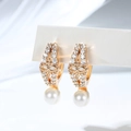 Macro shot of gold-plated hoop earrings with micro-set zircons and a white pearl drop - Symmetrical Hollow Pattern (EH877)