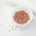 Macro-opname van roségouden ronde kralen in een witte kom voor het maken van DIY-sieraden - 2mm / Roségoud