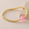 Pulsera elástica de cuentas doradas con colgante de cruz rosa sobre una piedra natural - Rosa