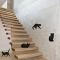 Detail of four black cat mirror wall stickers in various poses on a grey staircase wall - Black