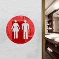 Red circular acrylic restroom sign with cutout icons on a white textured wall - Red