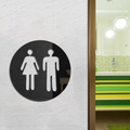 Rond zwart toiletbord met man- en vrouwsymbolen op een witte getextureerde muur - Zwart