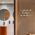 Détail d'un autocollant miroir argenté Toilet avec bordure décorative sur mur brun - Argenté