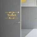 Détail de la plaque de toilette miroir dorée avec motifs à volutes sur une porte sombre - Doré