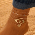 Detailed close-up of 5pcs layered gold anklet set with freedom charm on a sunny beach - Gold Handcuff Heart Crystal (7545)