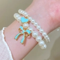 Detail von zweilagigen Perlenarmbändern mit blauem Herz und Bogenanhänger am Handgelenk - Grün (6579) / 2er Set