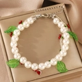 Detailed shot of pearl bracelet featuring green leaves and a red heart crystal charm - Cherry and Leaf Pendant Style / Cherry (8033)