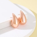 Close-up of polished rose gold teardrop stud earrings on minimalist display - Rose Gold