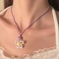 Nahaufnahme einer lila Kordelkette mit transparentem Blumenanhänger auf weißem Spitzenoutfit - Weiße Blume (Transparent)