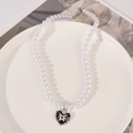 Close-up of pearl necklace with a black enamel heart pendant and pink cross detailing - Heart