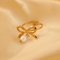 Dettaglio di un anello a fiocco dorato con perla bianca su sfondo di seta champagne - Anello con perla e fiocco dorato (10494)