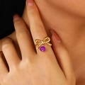 Nahaufnahme eines goldenen Schleifenrings mit lila Perlenanhänger an einer Hand - Schleife Ring (11438)