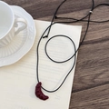 Detail der Croissant-Halskette auf einem rustikalen Holztisch mit einer Kaffeetasse - Rot