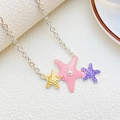 Dettaglio macro di ciondoli a stella marina rosa, gialla e viola con perla centrale - Collana di Perle Stella Marina Tricolore (12430)