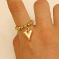 Bague perlée dorée avec pendentif cœur poli présentée sur le doigt d'un mannequin - Bague Cœur Or 0182
