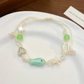 Close-up of ocean-style ceramic beads with sea shell and fish charms on a woven cord - Silver Green