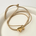 Minimalistisches beiges Flechtarmband mit goldenem Pony-Anhänger auf weißem Keramiktablett - KC Gold Geflochtener Seilstil