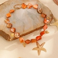 Dettaglio della collana di conchiglie arancioni con ciondoli a stella marina dorata su sabbia - Collana di Conchiglia Arancione (G-237)
