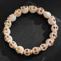 Gros plan d'un bracelet de perles tête de mort avec gravures sur pierre sombre - Crâne de Couleur Crème